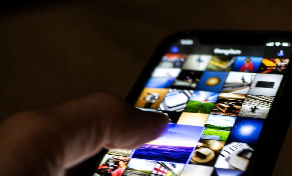 A finger selecting multiple iPhone photos at once by dragging diagonally across the screen.