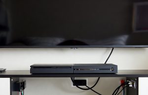 Cable Chaos Tamer: Organize Wires with Household Items Behind a TV console, cables are managed invisibly using clear adhesive hooks mounted on the furniture back.