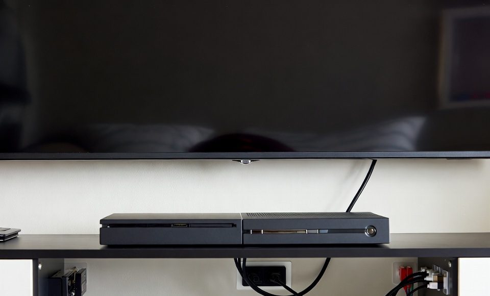 Behind a TV console, cables are managed invisibly using clear adhesive hooks mounted on the furniture back.